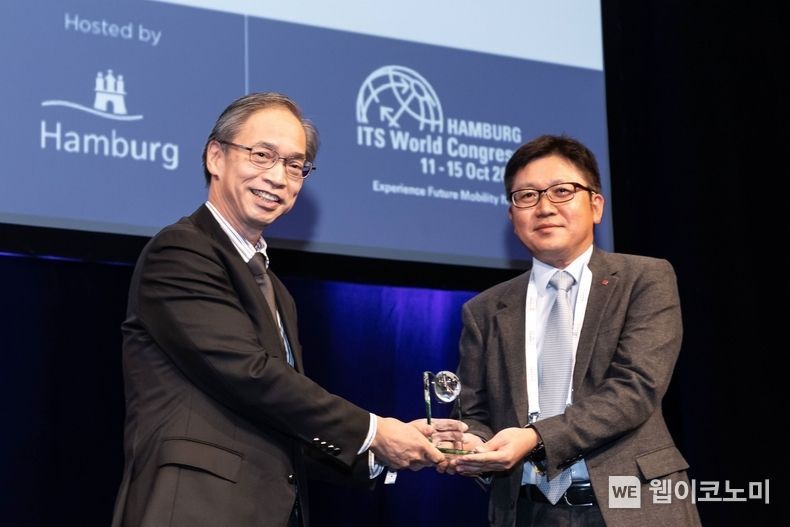 LG유플러스는 지난 11~15일 독일 함부르크 메세(Hamburg Messe)에서 열린 제27회 ITS 세계총회에서 ‘기업 부문 명예의 전당상(공로상)’을 받았다고 17일 밝혔다. 사진은 ITS 세계총회 중 운영된 ‘한국관’과 조원석 LG유플러스 기업신사업그룹장(전무, 오른쪽)이 아마노 하지메 ITS 아태사무국 사무총장으로부터 기업 부문 명예의 전당상을 받고 있는 모습. 2021.1017 (출처 = LG유플러스)