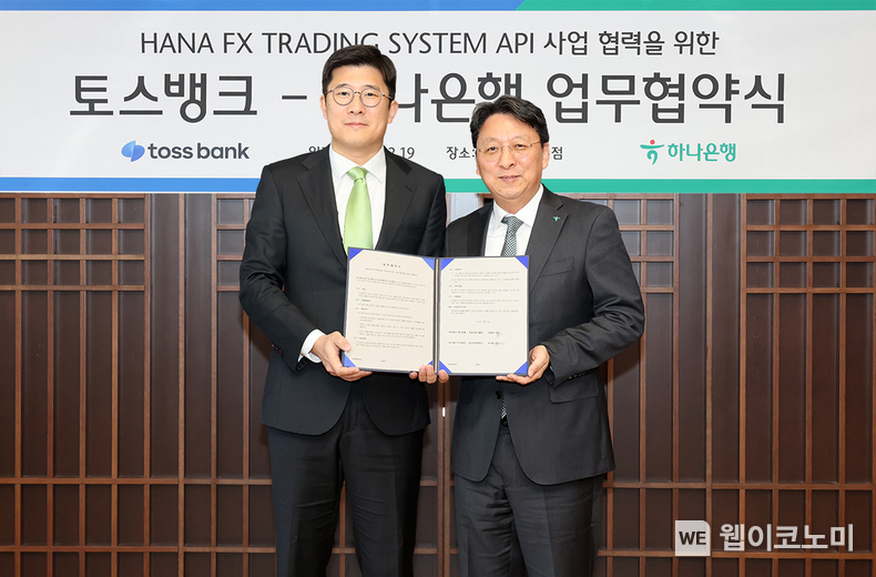 하나은행은 19일 오전 을지로 본점에서 토스뱅크와 실시간 환율을 적용한 『24시간 다통화 FX 거래』 활성화를 위한 업무협약을 체결했다. 협약식에 참석한 남궁원 하나은행 자금시장그룹 부행장(사진 오른쪽)과 김지웅 토스뱅크 최고전략책임자(사진 왼쪽)가 협약서를 들고 기념촬영을 하고 있다. / 2023.12.19 (출처: 하나은행)
