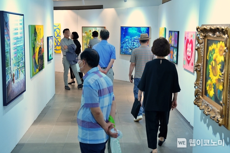 올아트페어 포스터와 '롯데마트 송파점 2층 상설 미술품 매장에서 작품을 구경하고 있는 방문객들의 모습' / 2024.10.28 (출처: 롯데쇼핑)