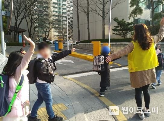 어린이들이 교통안전지도사와 함께 등교하고 있다.